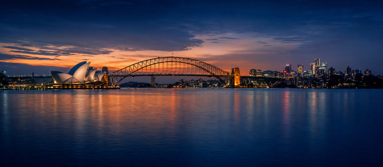 Sydney Harbour at twilight with city lights coming on across the water